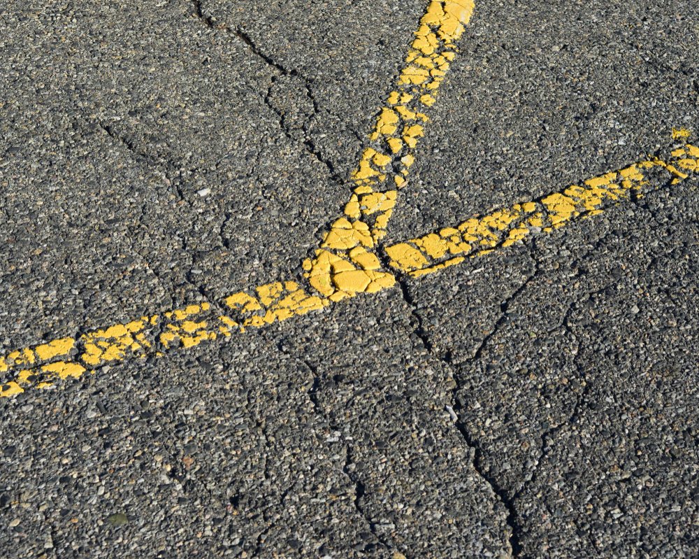 Close-Up Of Yellow Cracked Road Markings On An Aging Asphalt Surface, Showing Signs Of Wear And Deterioration